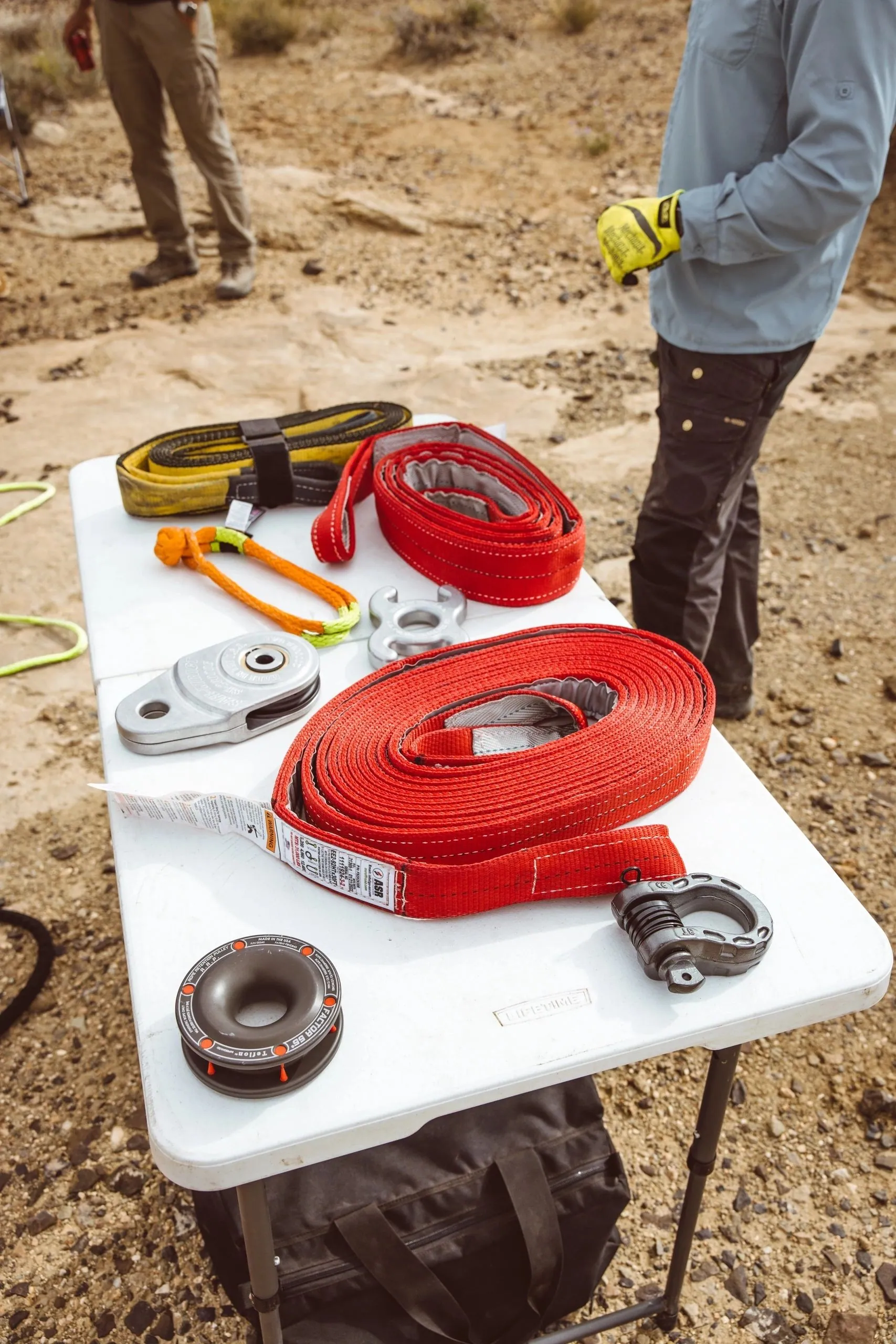 Recovery gear laid out on a folding table on the trail: red straps, shackles and a snatch block