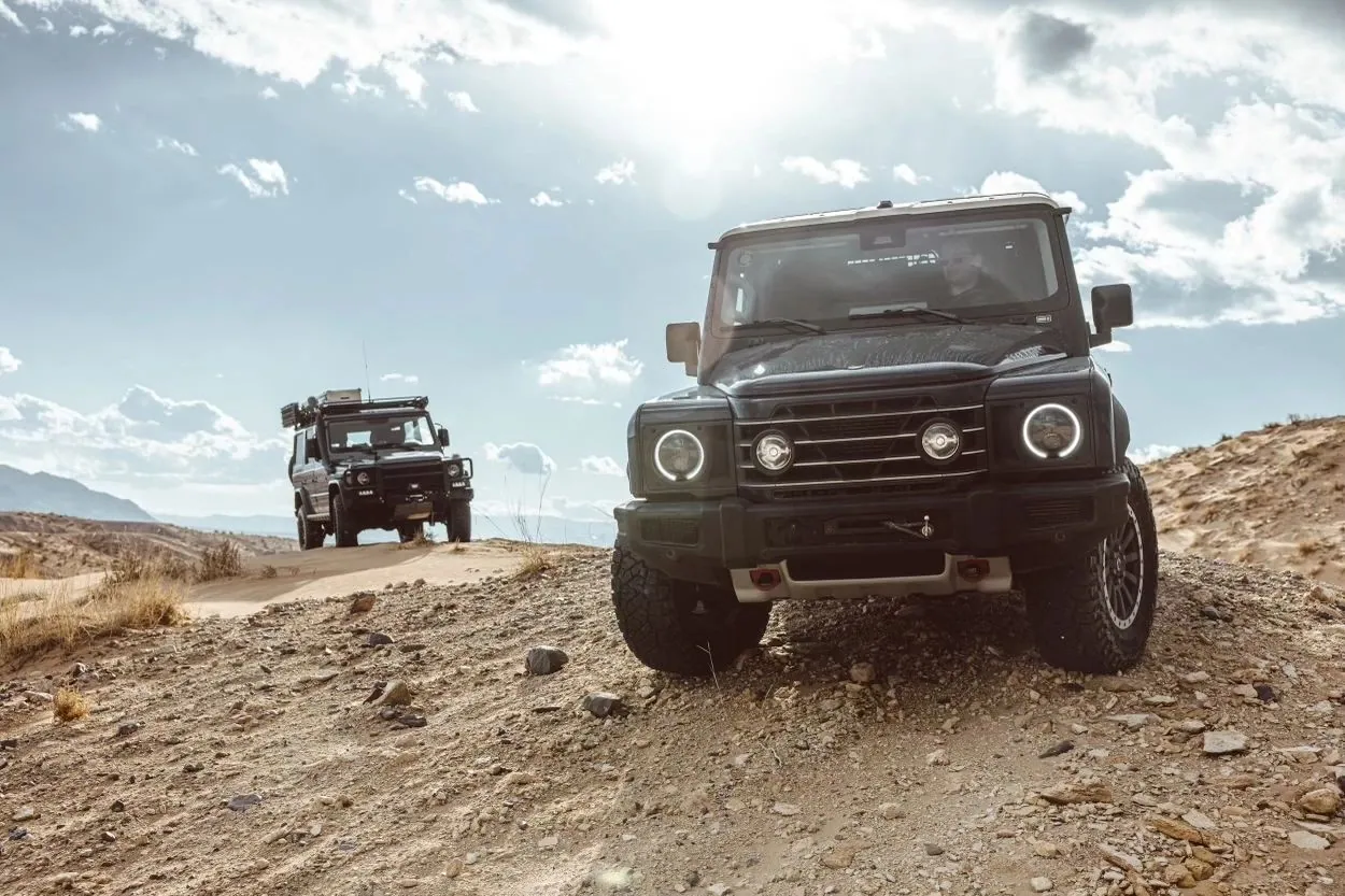Two black 4x4s on a dirt track in the desert hills under a bright sky