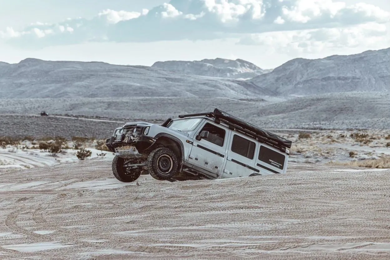 White 4x4 tilted in a muddy rut on a desert flat, mountains behind