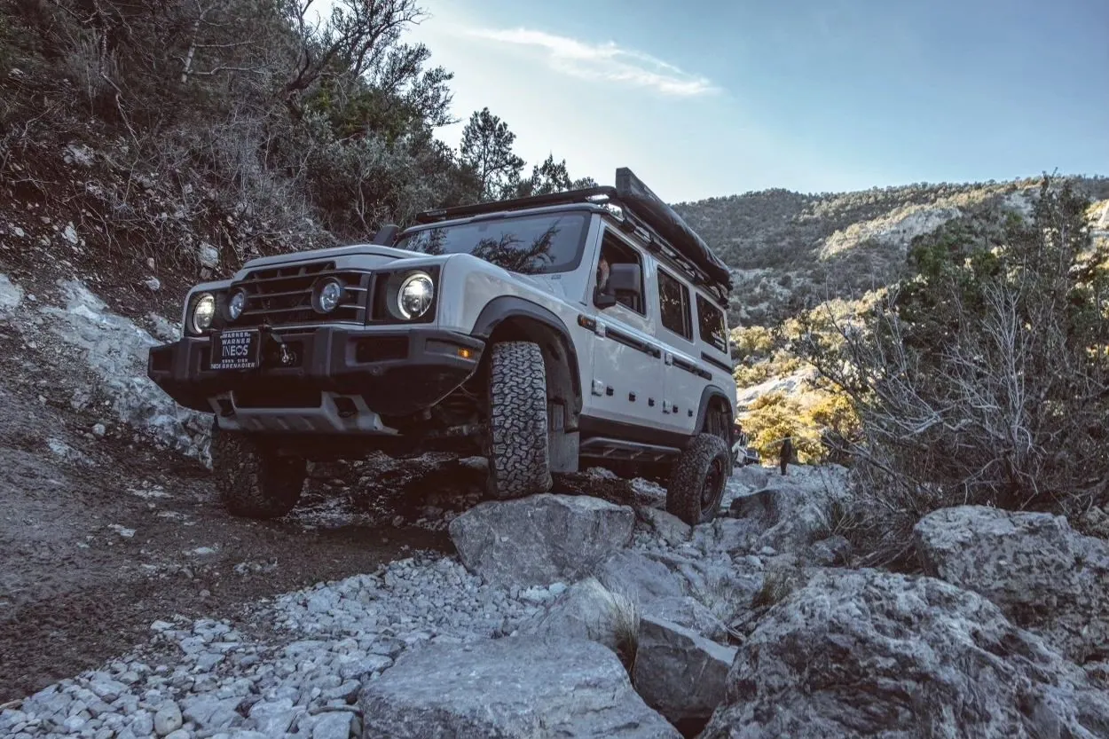 Silver 4x4 crawling over boulders on a rocky trail among pines