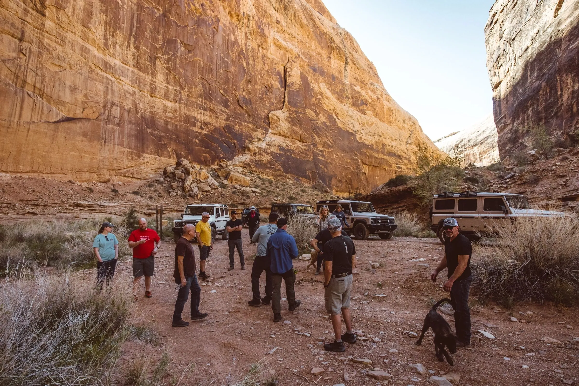 Guests standing together on a red sandstone canyon floor with vehicles parked behind