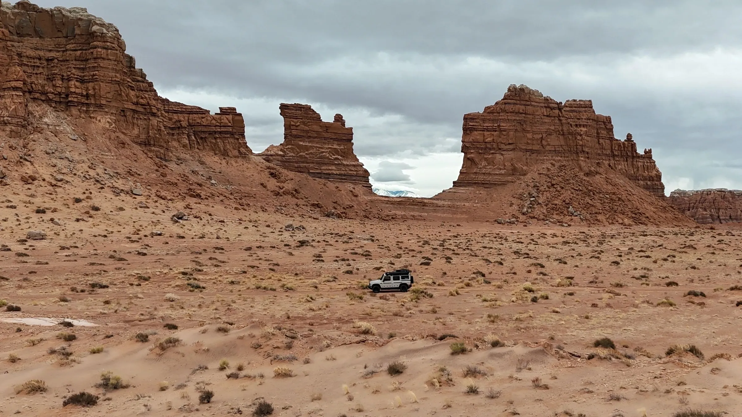 Drone view of a lone vehicle below red rock buttes in open desert