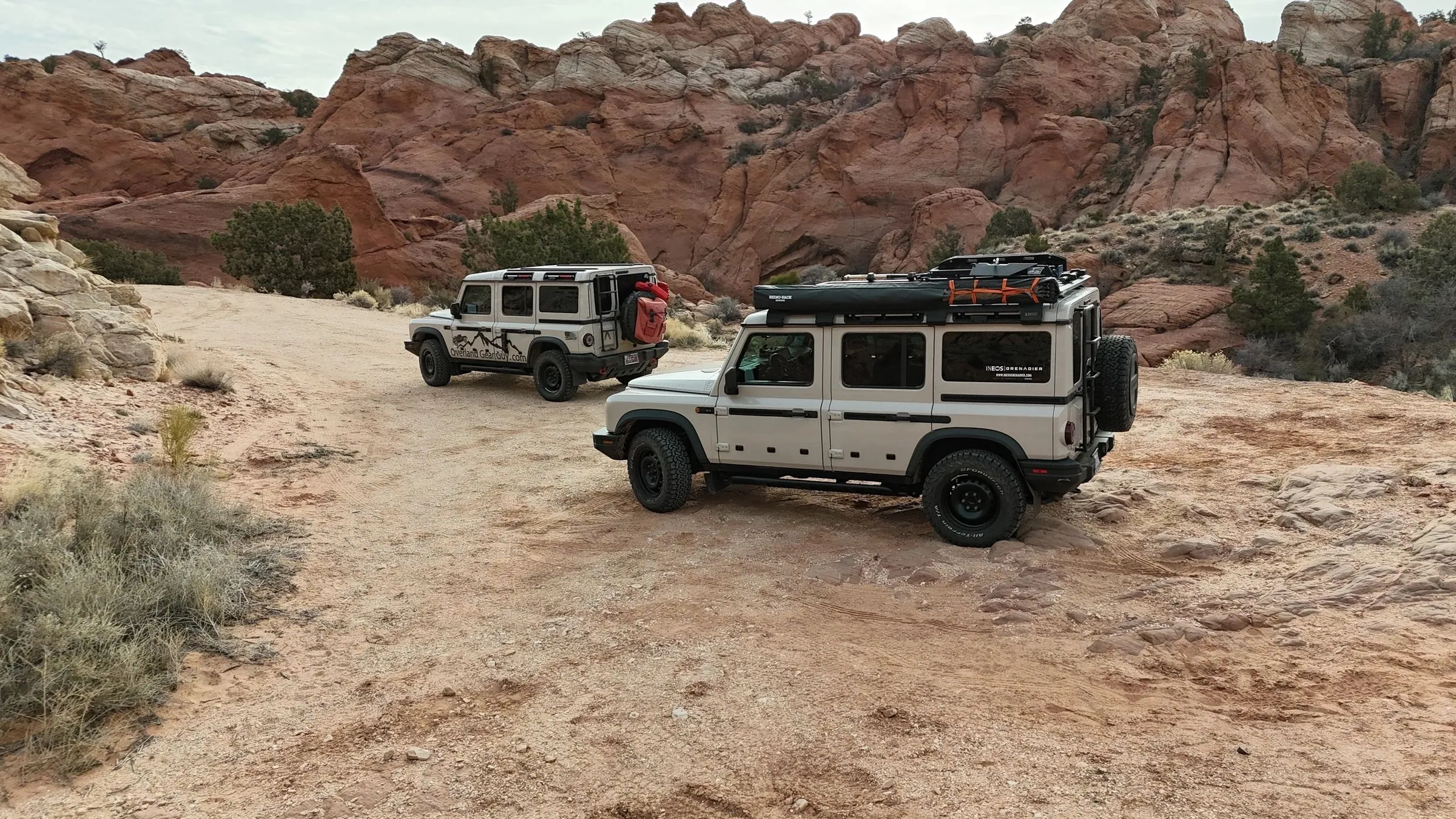 Two 4x4s on a slickrock trail beneath red cliffs