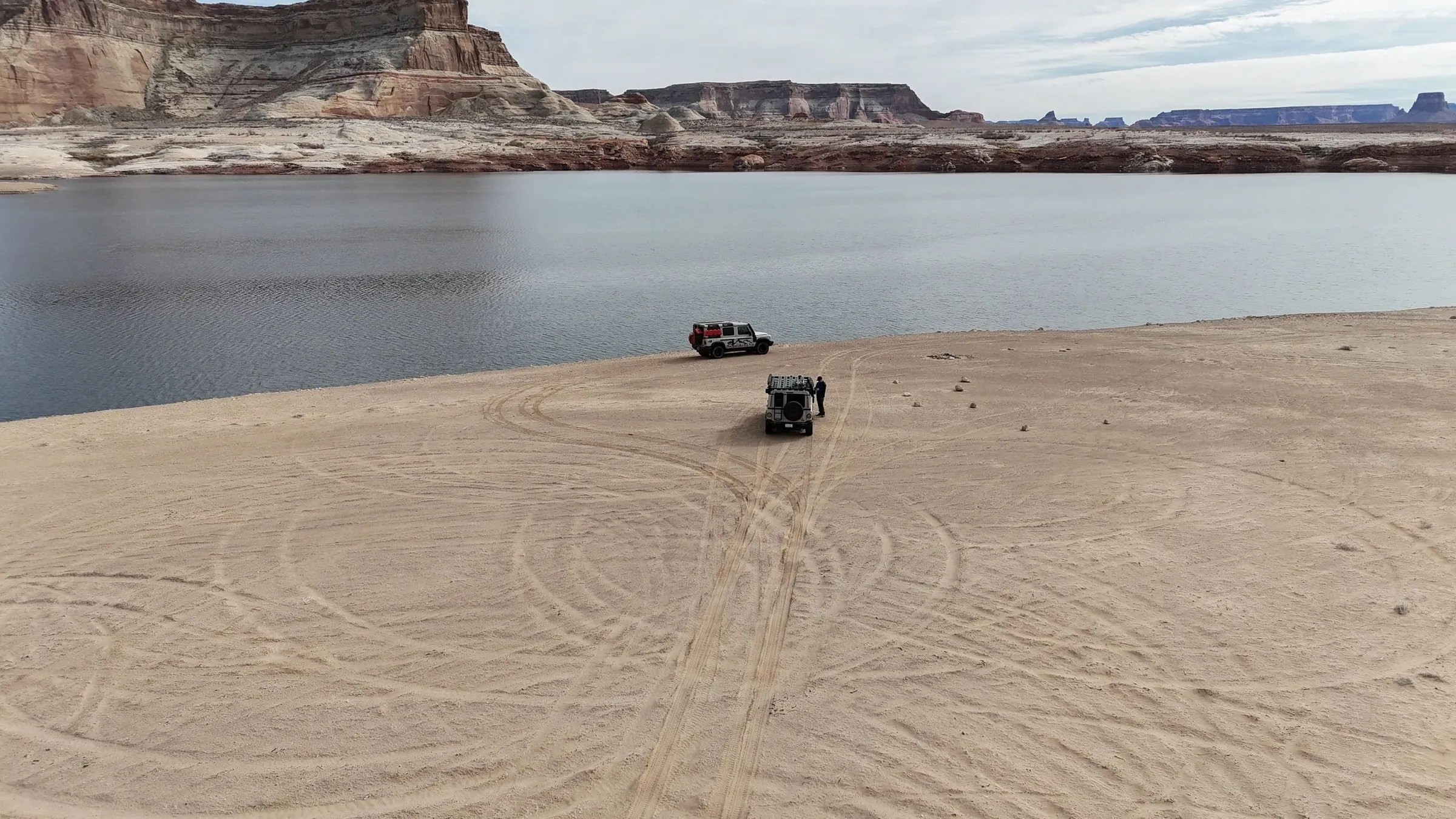 Aerial view of vehicles on a sandy lakeshore with mesas across the water