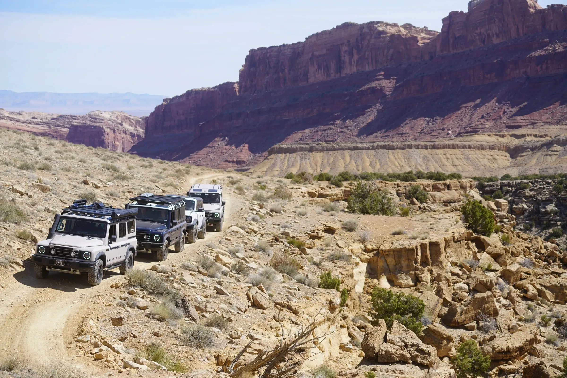 Line of 4x4s on a dirt road winding below canyon walls
