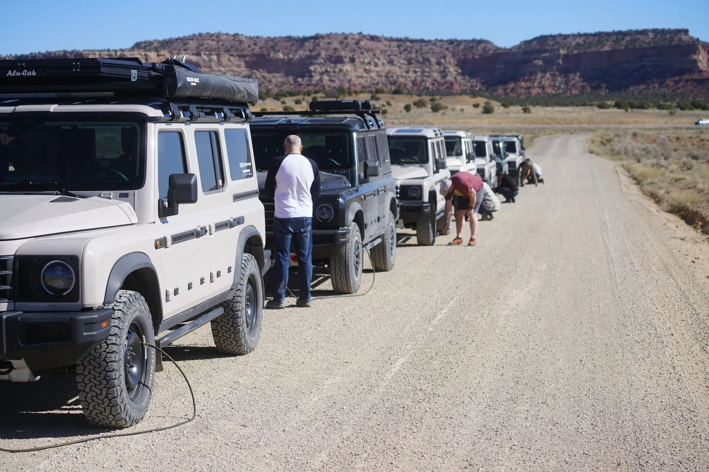 Row of 4x4s parked along a gravel road as drivers check their vehicles