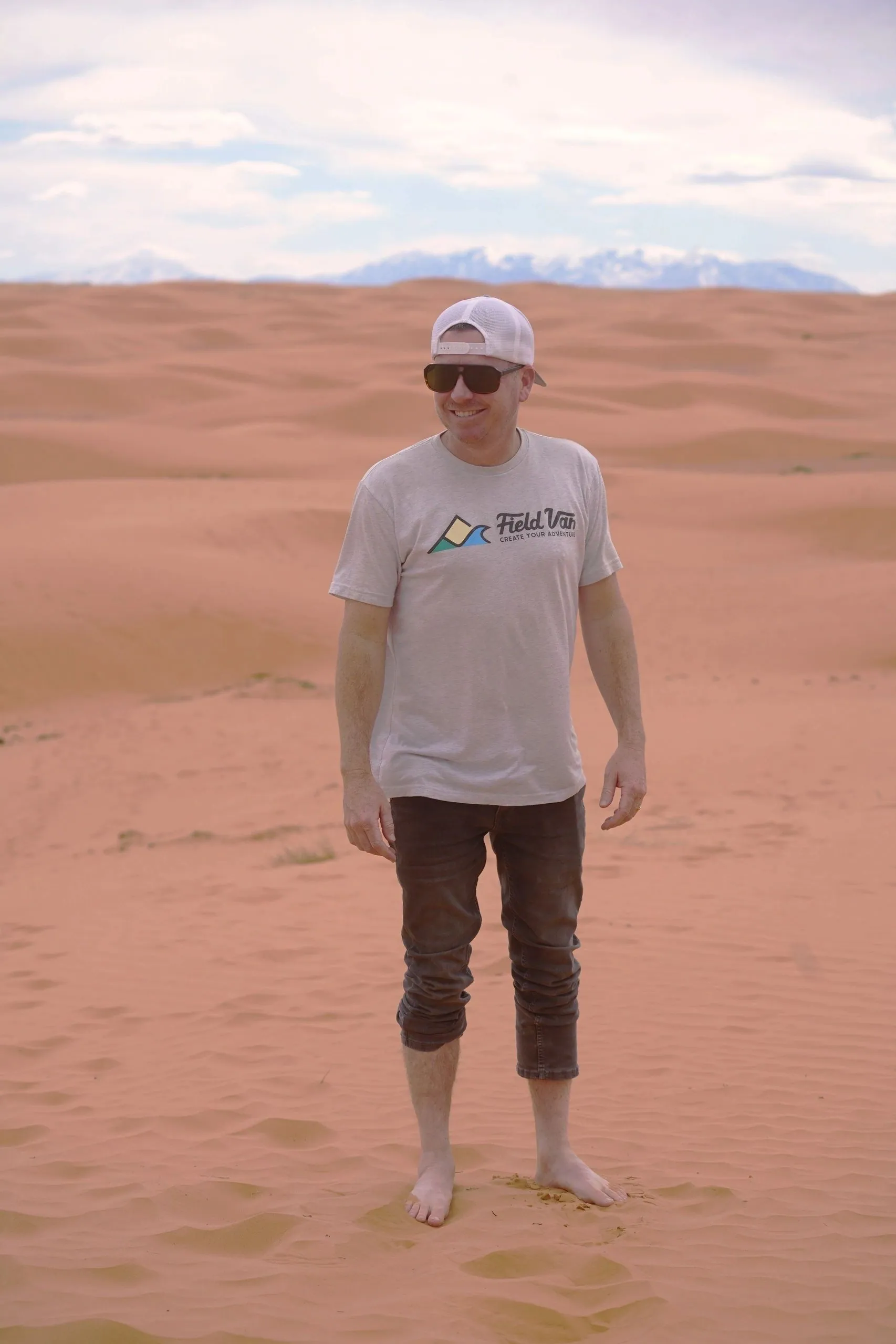 Guest standing barefoot on red sand dunes with snowy mountains behind