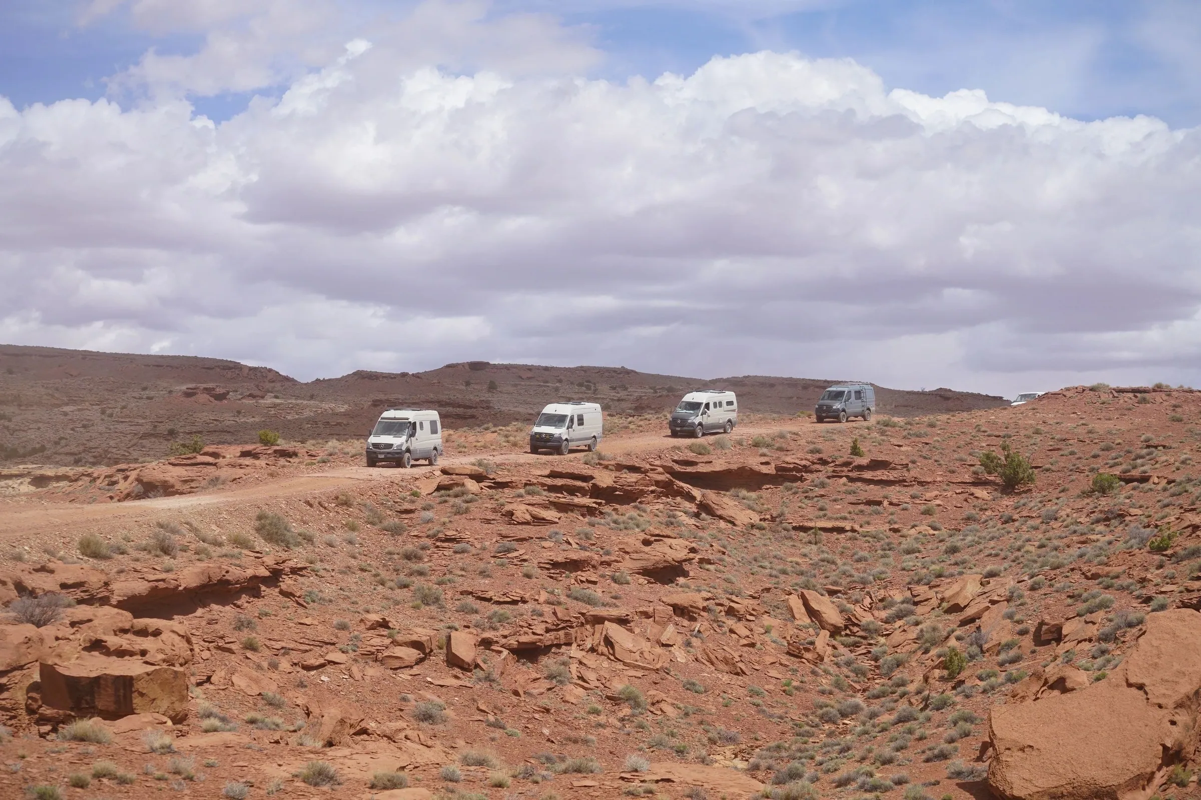 Convoy of camper vans crossing red desert under big clouds