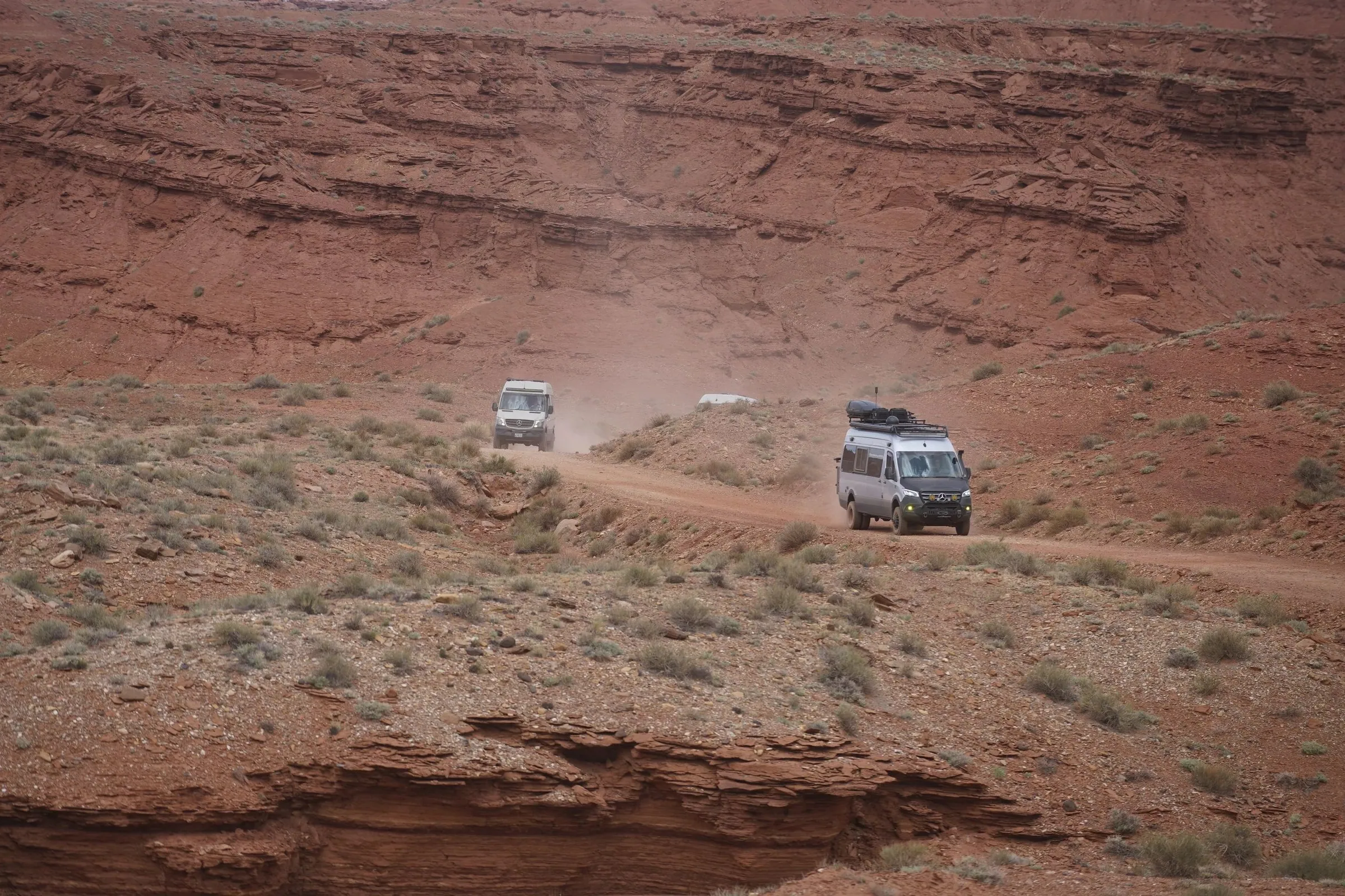 Two vans driving a dirt road across red desert slopes