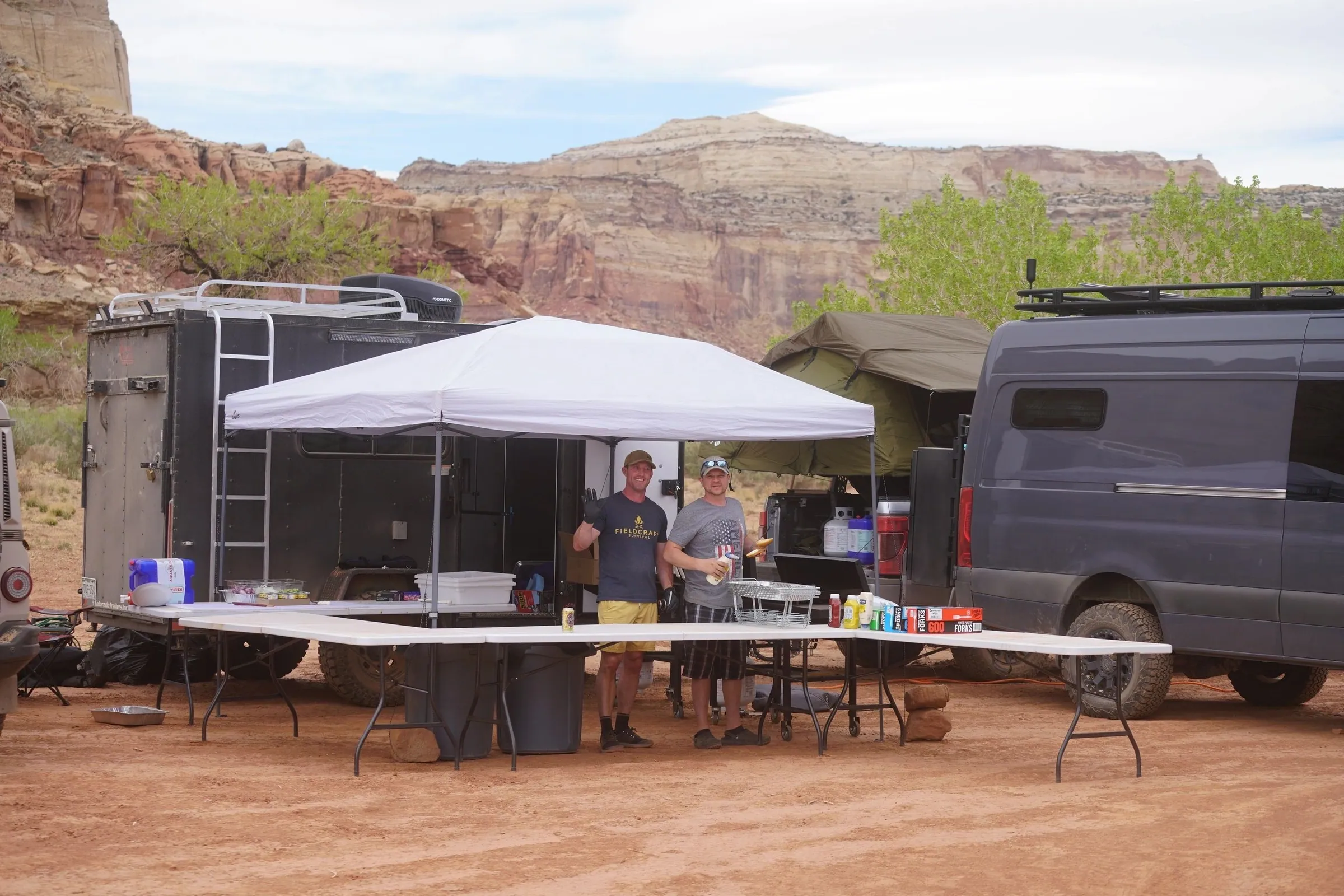 Camp kitchen under a canopy beside camper vans