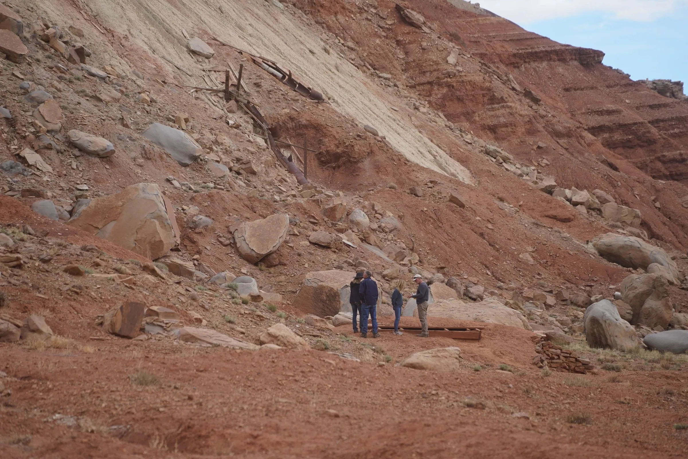 Small group hiking a trail below eroded red slopes