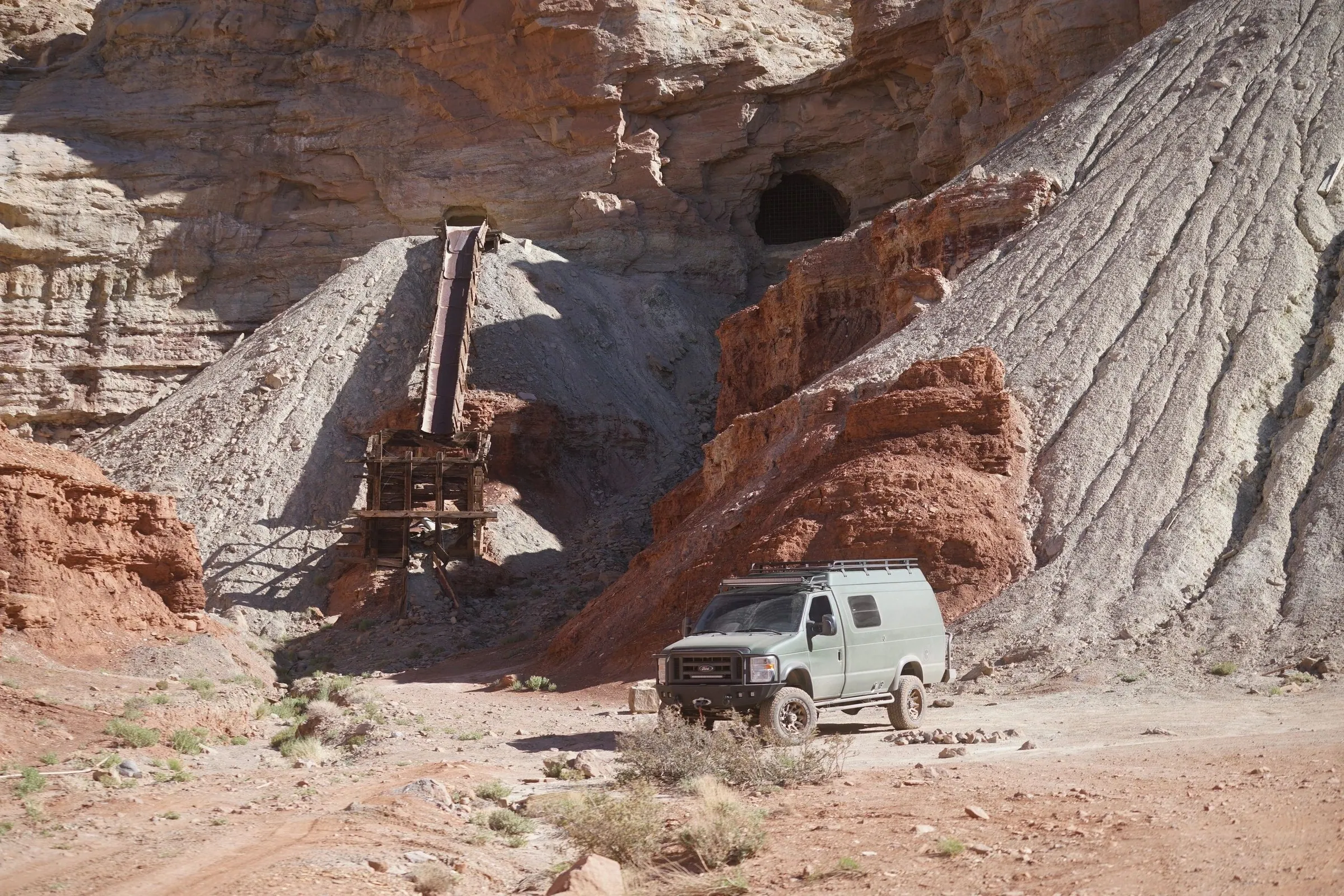 Van parked below a striped rock formation and an old mine structure
