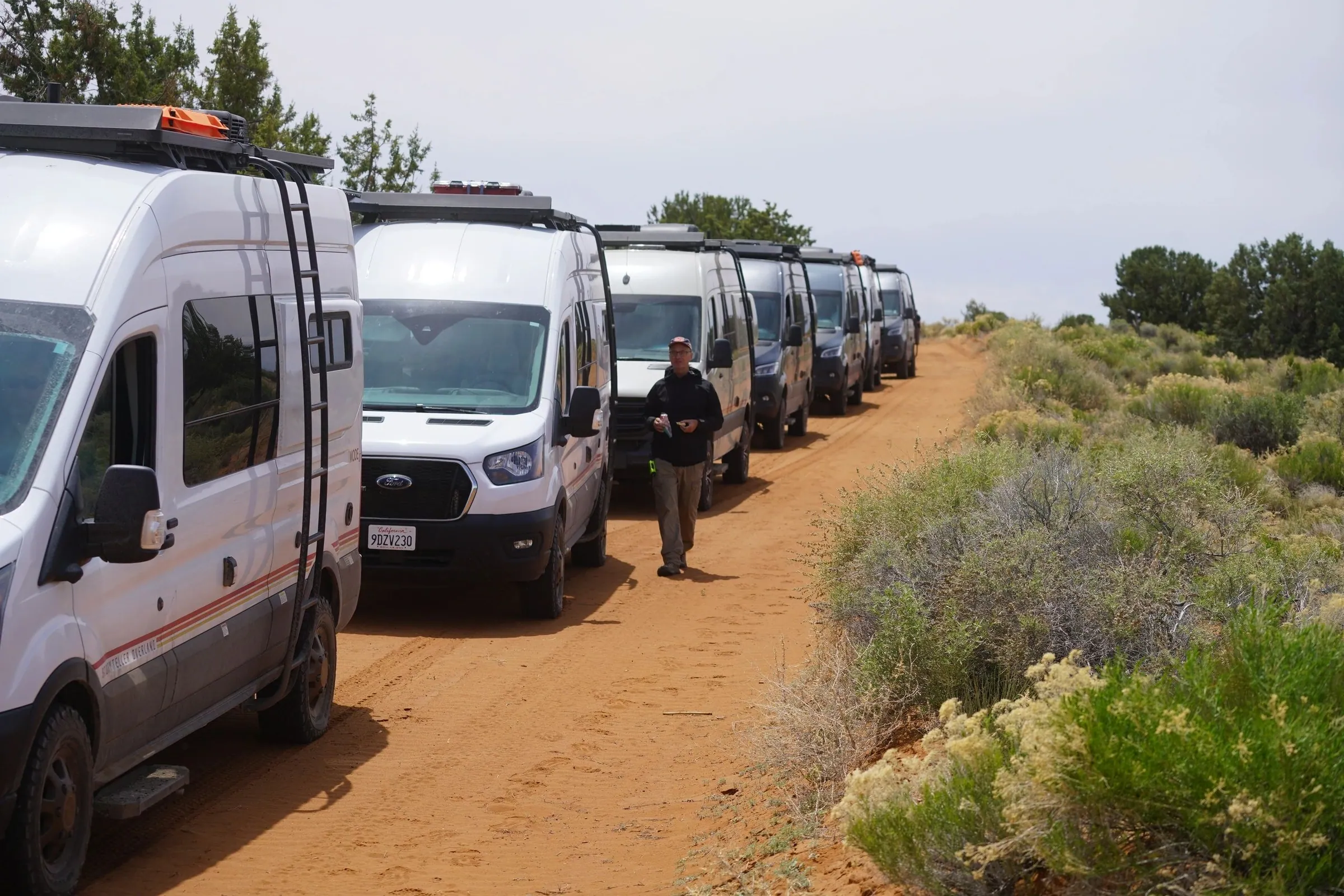 Line of camper vans parked along a sandy road through sagebrush