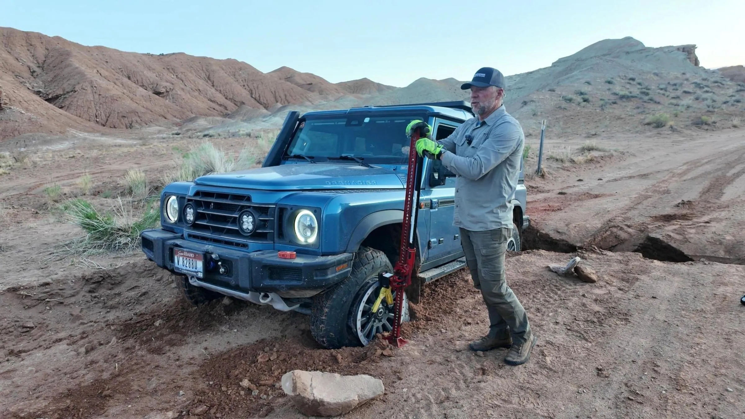 Instructor rigging a recovery strap to a blue 4x4 stuck on a desert slope