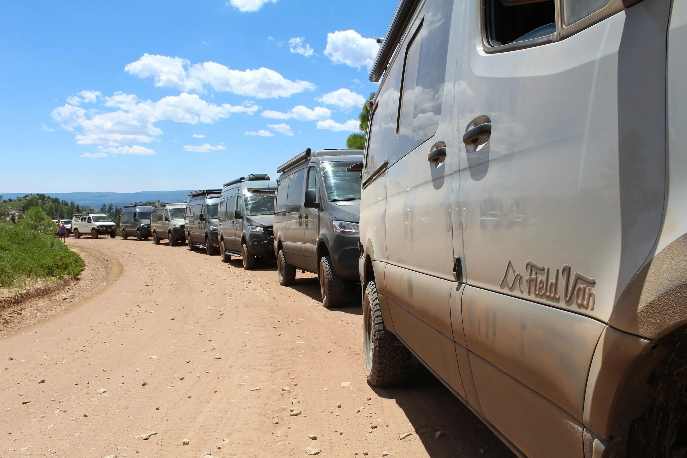 Row of camper vans along a dirt road, Field Van logo on the nearest