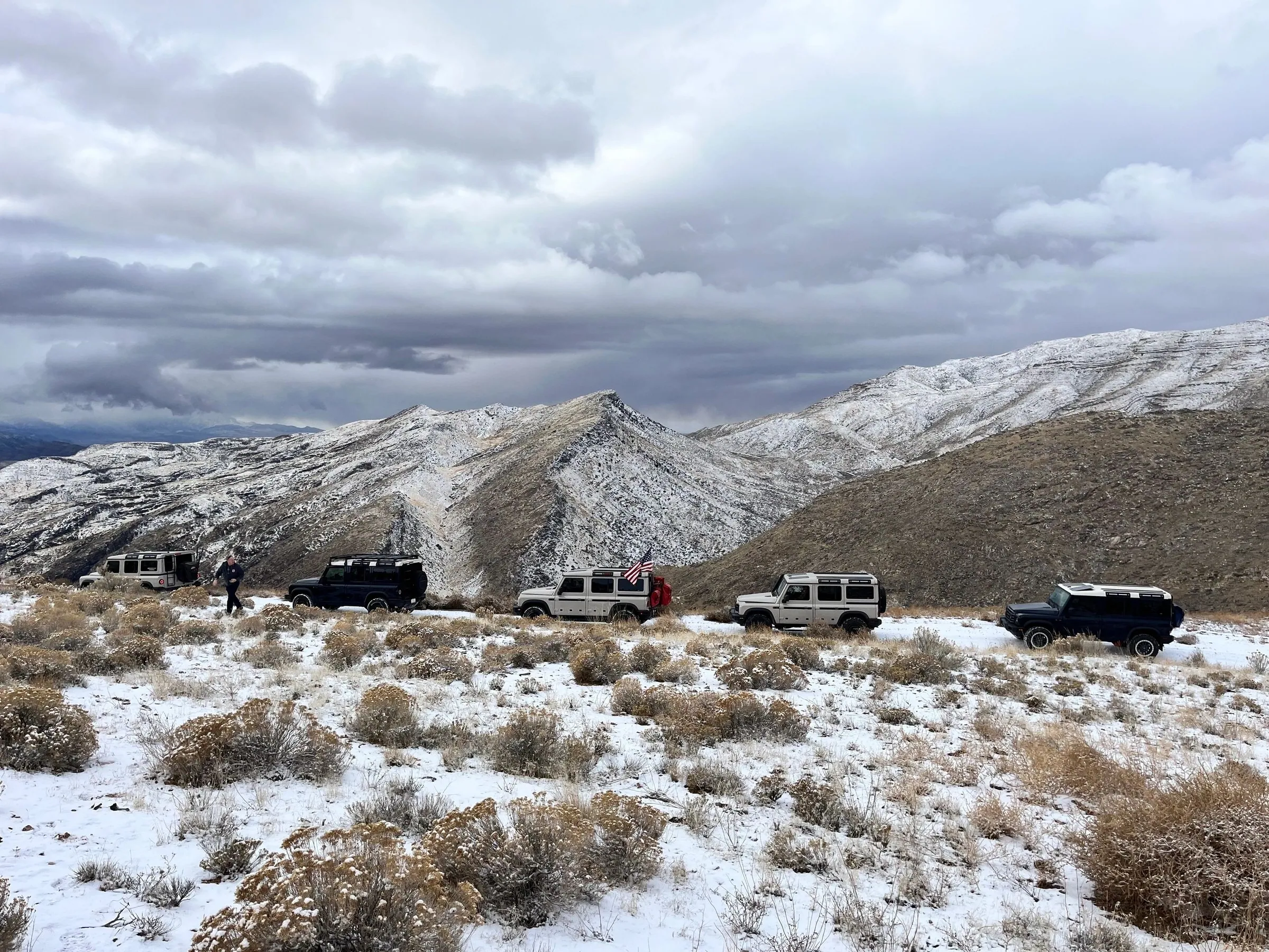4x4s lined up on a snowy ridge under heavy clouds