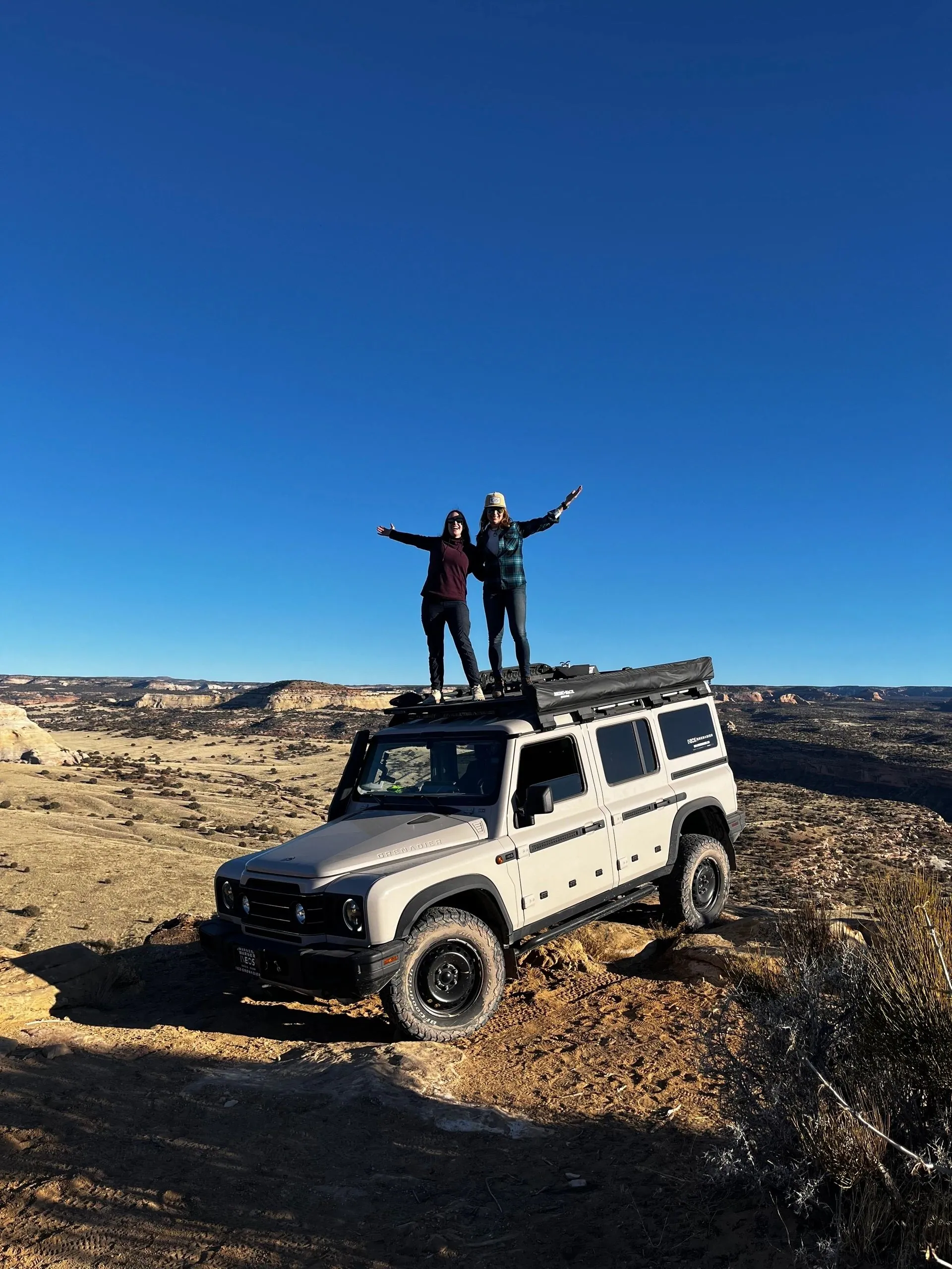 Two people standing on a 4x4 roof above canyon country