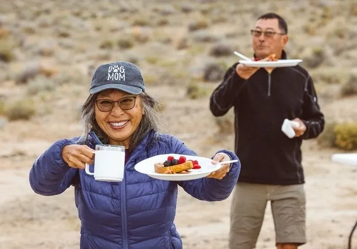 Smiling guests holding breakfast plates and coffee at camp