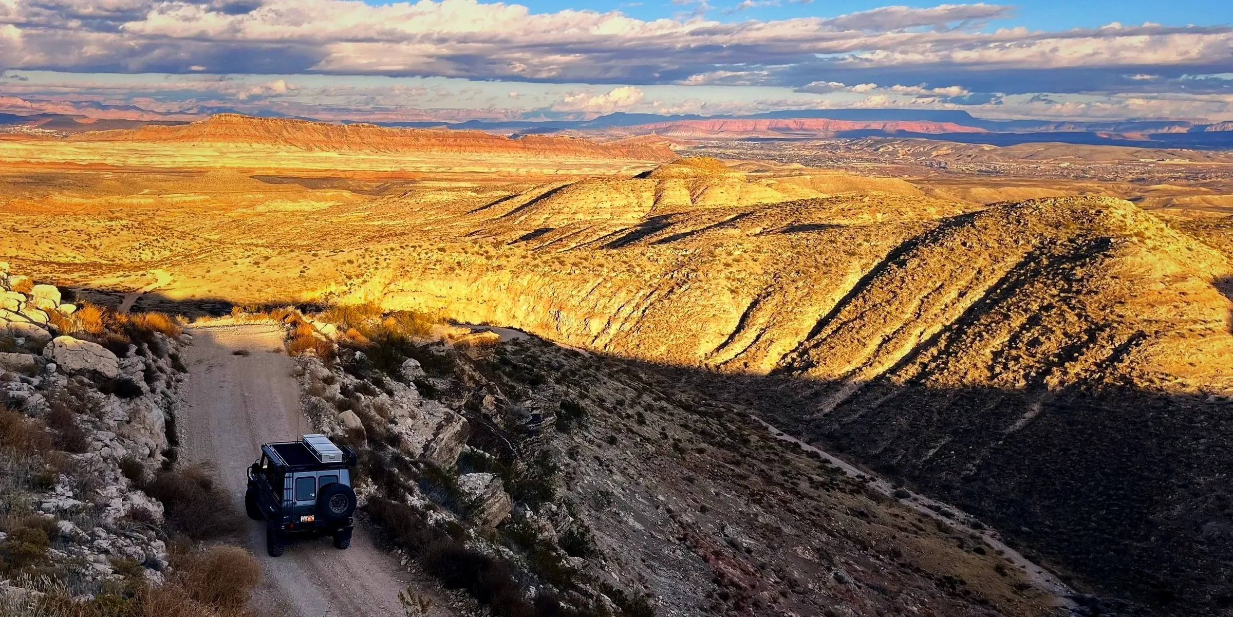 Vehicle descending a dirt road above golden canyon slopes